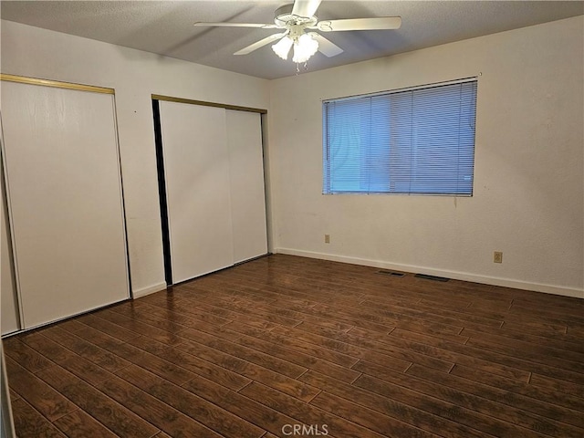 unfurnished bedroom featuring baseboards, wood finished floors, visible vents, and multiple closets