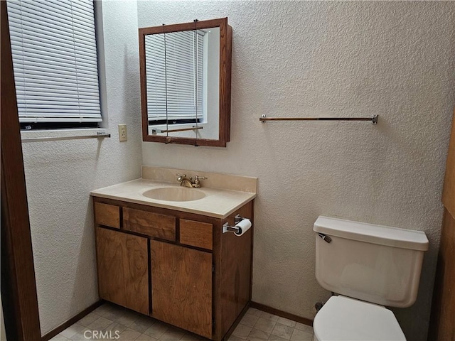 half bath with baseboards, a textured wall, vanity, and toilet