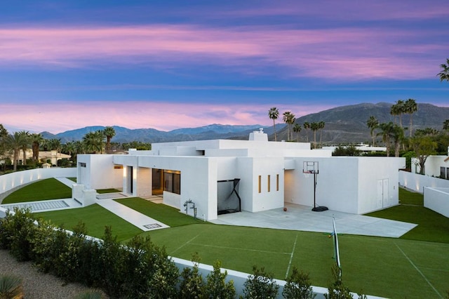 back house at dusk featuring a lawn and a mountain view