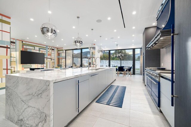 kitchen with a large island with sink, white cabinets, sink, stainless steel stove, and hanging light fixtures