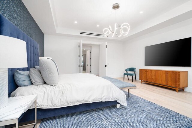 bedroom featuring wood-type flooring, an inviting chandelier, and a tray ceiling