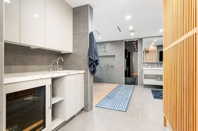 kitchen featuring light tile patterned floors, white cabinetry, beverage cooler, light stone countertops, and sink