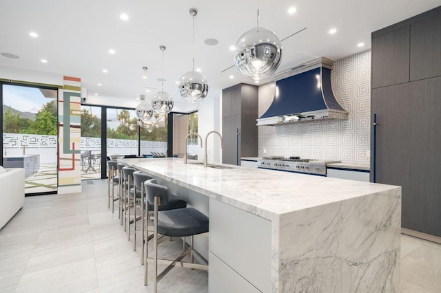 kitchen featuring a spacious island, stove, wall chimney range hood, pendant lighting, and sink