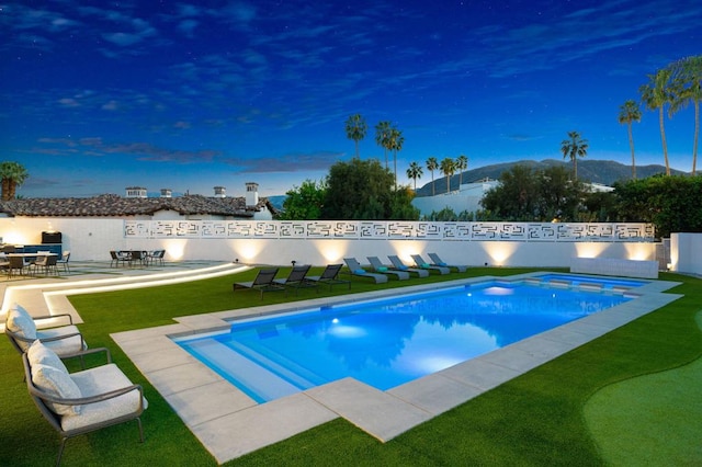 pool at dusk with a patio area, a yard, and a mountain view