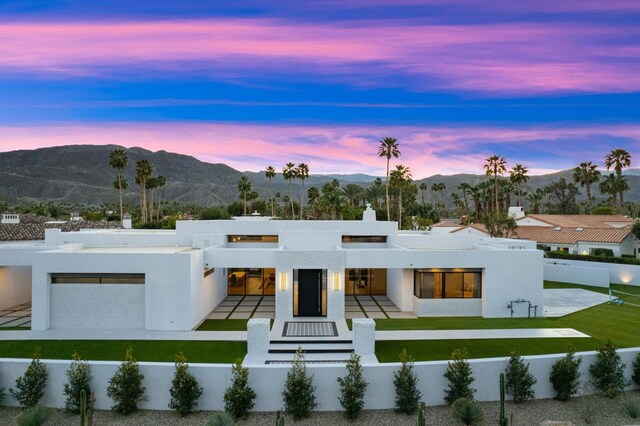 back house at dusk featuring a mountain view, a yard, and a garage