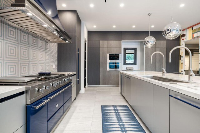 kitchen featuring appliances with stainless steel finishes, wall chimney exhaust hood, sink, hanging light fixtures, and light stone counters