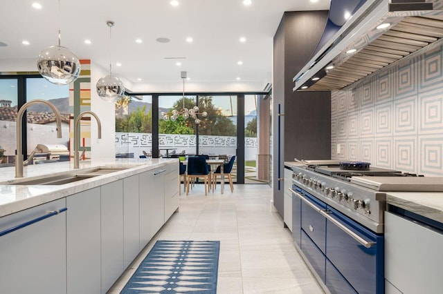 kitchen with light stone countertops, pendant lighting, wall chimney exhaust hood, stainless steel appliances, and sink