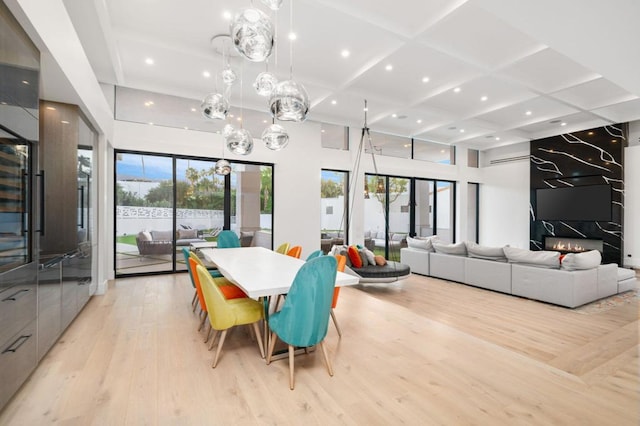 dining space with a fireplace, a wealth of natural light, light hardwood / wood-style flooring, and coffered ceiling