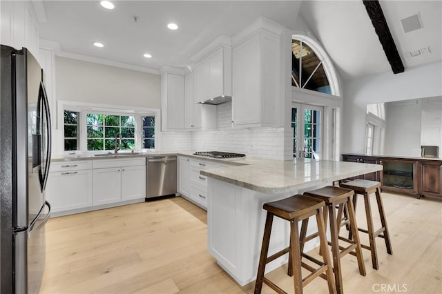 kitchen featuring white cabinetry, kitchen peninsula, a breakfast bar area, stainless steel appliances, and tasteful backsplash