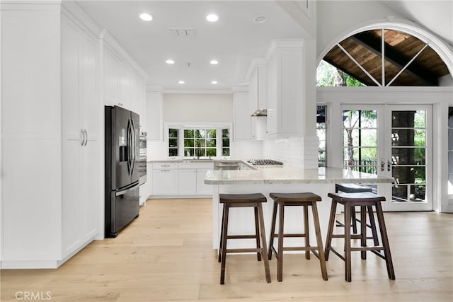 kitchen featuring kitchen peninsula, backsplash, black fridge, a kitchen breakfast bar, and white cabinets