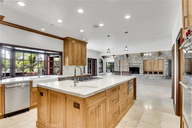 kitchen with pendant lighting, appliances with stainless steel finishes, sink, a kitchen island with sink, and light stone counters