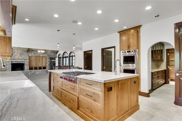 kitchen featuring sink, hanging light fixtures, appliances with stainless steel finishes, and a center island with sink