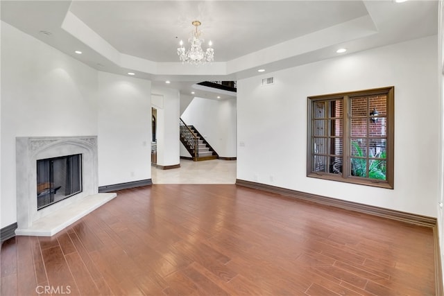 unfurnished living room with a raised ceiling, wood-type flooring, a fireplace, and a notable chandelier