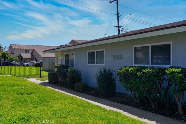 view of side of home with a lawn, fence, and stucco siding