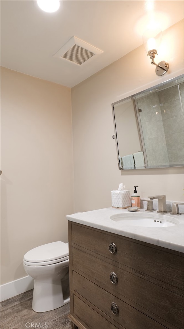 bathroom with toilet, wood finished floors, visible vents, vanity, and baseboards