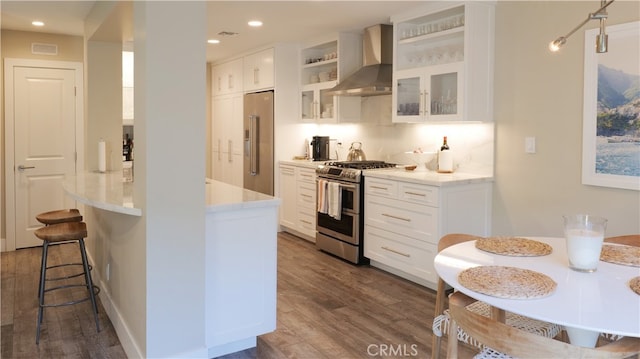 kitchen with a breakfast bar area, stainless steel appliances, white cabinets, dark wood-style floors, and wall chimney exhaust hood