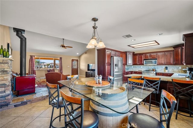 dining space featuring light tile patterned floors, vaulted ceiling, a wood stove, and ceiling fan