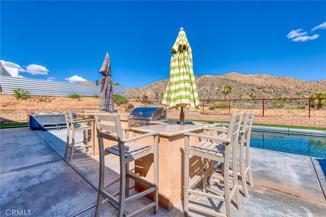 view of patio / terrace with a mountain view, a fenced in pool, grilling area, exterior kitchen, and a bar