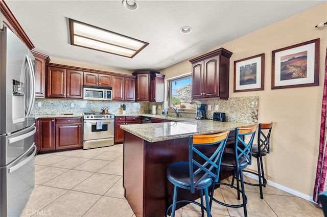 kitchen with tasteful backsplash, light stone counters, kitchen peninsula, a kitchen bar, and appliances with stainless steel finishes