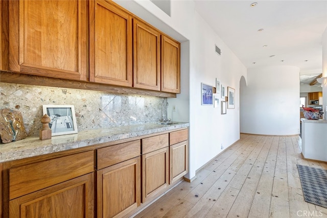 kitchen with backsplash, light stone countertops, sink, and light wood-type flooring