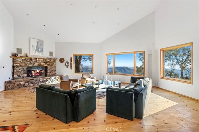 living room featuring a stone fireplace, a mountain view, high vaulted ceiling, and light wood-type flooring