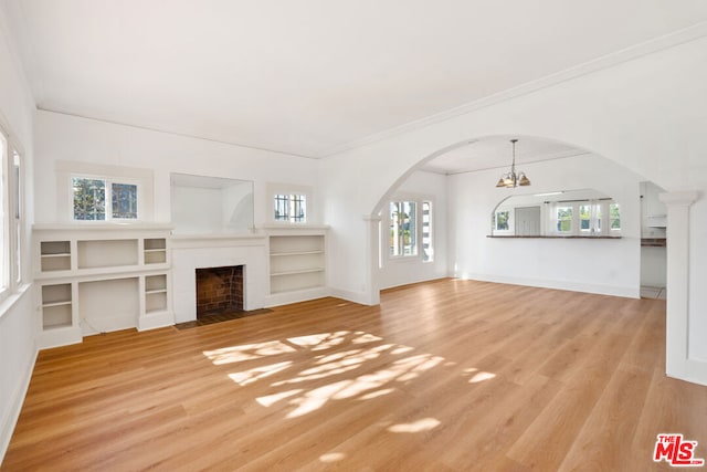 unfurnished living room with built in features, light hardwood / wood-style flooring, ornamental molding, and an inviting chandelier