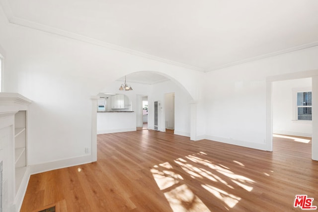 unfurnished living room featuring hardwood / wood-style floors, crown molding, and an inviting chandelier