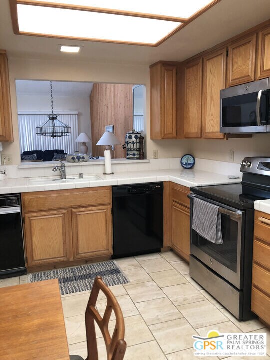 kitchen with stainless steel appliances, sink, pendant lighting, tile counters, and light tile patterned floors