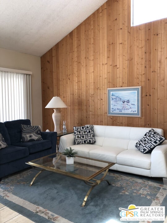 living room with a textured ceiling, wooden walls, lofted ceiling, and a wealth of natural light