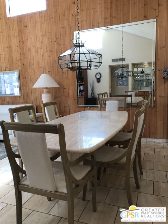 tiled dining area featuring a notable chandelier, wood walls, and vaulted ceiling