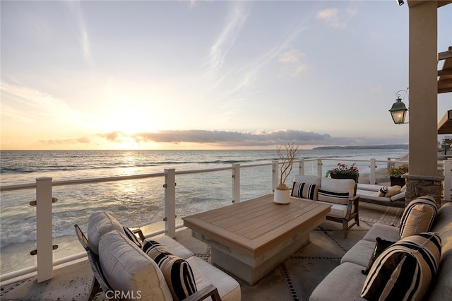 balcony at dusk with a view of the beach, a water view, and an outdoor hangout area