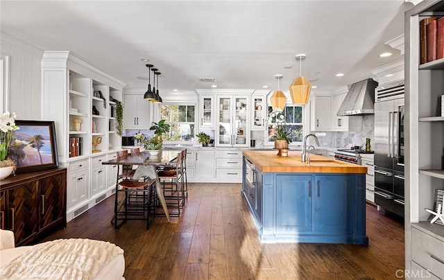 kitchen with hanging light fixtures, white cabinetry, wall chimney exhaust hood, wooden counters, and a center island