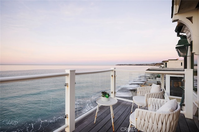 balcony at dusk featuring a water view