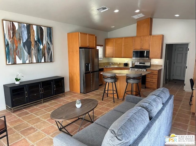 kitchen featuring a breakfast bar, a center island, vaulted ceiling, light tile patterned flooring, and stainless steel appliances