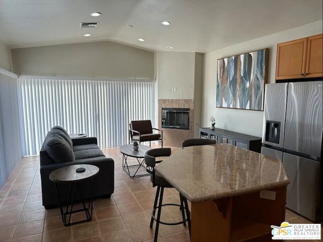 kitchen featuring stainless steel fridge with ice dispenser, lofted ceiling, a breakfast bar area, a tiled fireplace, and a kitchen island