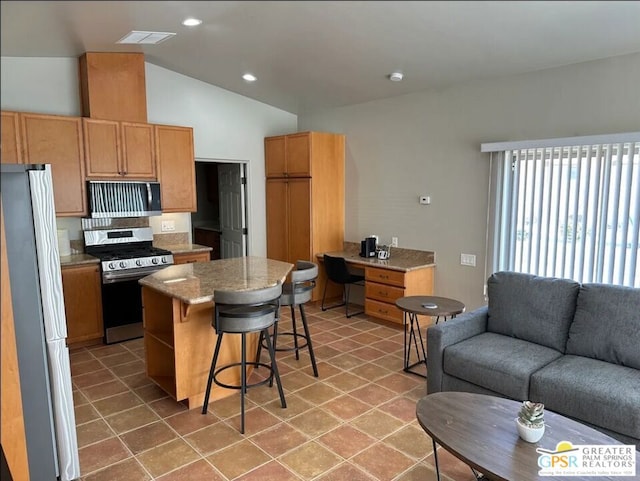 kitchen with a kitchen breakfast bar, light stone counters, lofted ceiling, a kitchen island, and appliances with stainless steel finishes