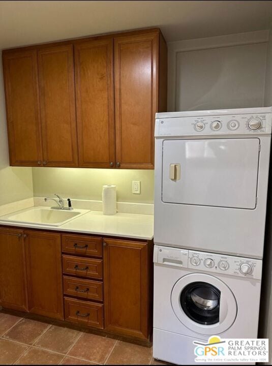 laundry room with cabinets, light tile patterned floors, stacked washer and dryer, and sink