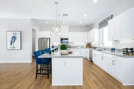 kitchen with white cabinetry, light wood-type flooring, stainless steel appliances, decorative light fixtures, and a center island