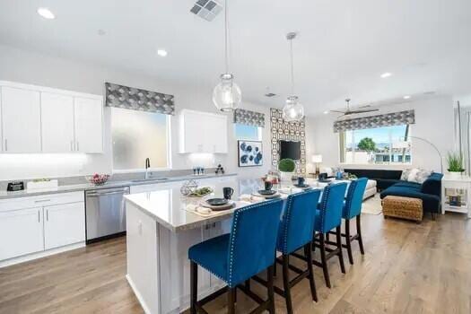 kitchen featuring a center island, white cabinetry, pendant lighting, stainless steel dishwasher, and light hardwood / wood-style flooring