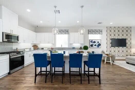 kitchen with appliances with stainless steel finishes, dark hardwood / wood-style flooring, white cabinetry, and pendant lighting