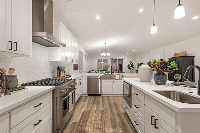 kitchen with wall chimney exhaust hood, stainless steel appliances, white cabinets, hanging light fixtures, and lofted ceiling