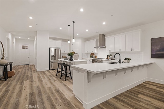 kitchen with a kitchen bar, stainless steel appliances, sink, wall chimney range hood, and white cabinets