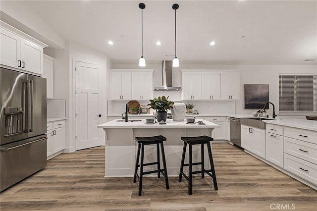 kitchen featuring stainless steel appliances, sink, wall chimney range hood, a center island with sink, and light hardwood / wood-style flooring