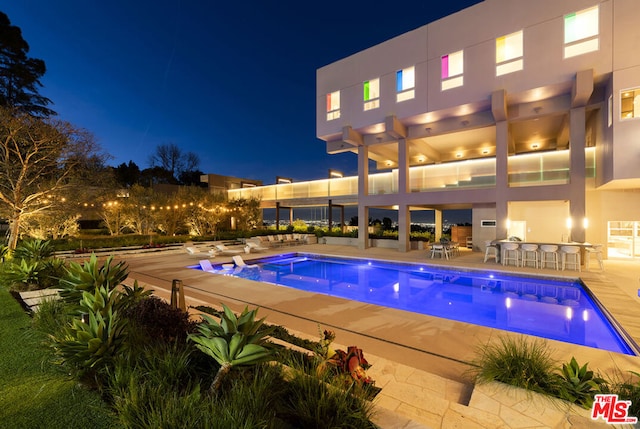 pool at night featuring a patio and a pergola