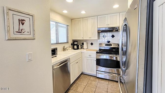 kitchen featuring decorative backsplash, appliances with stainless steel finishes, sink, light tile patterned floors, and white cabinetry