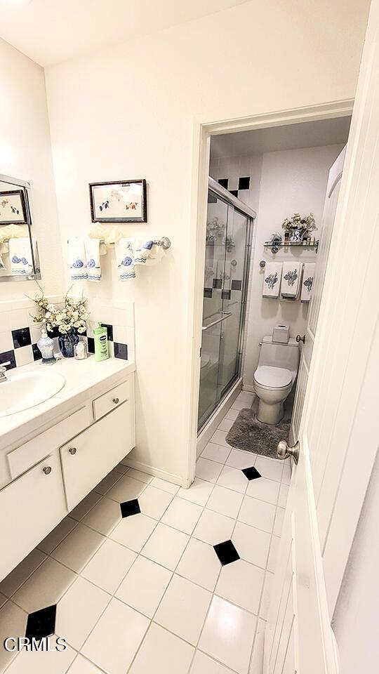 bathroom featuring toilet, vanity, tile patterned floors, and a shower with shower door