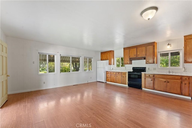 kitchen with black electric range, white fridge, a healthy amount of sunlight, and light wood-type flooring