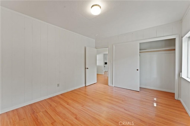 unfurnished bedroom featuring wooden walls, a closet, and light hardwood / wood-style floors