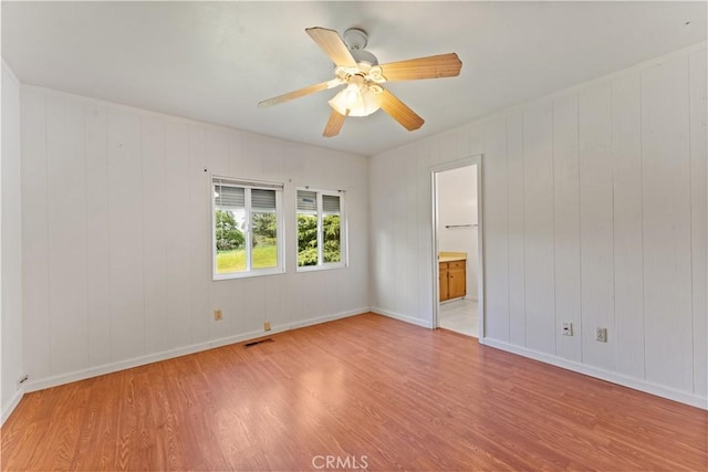 empty room with ceiling fan, light wood-type flooring, and wooden walls