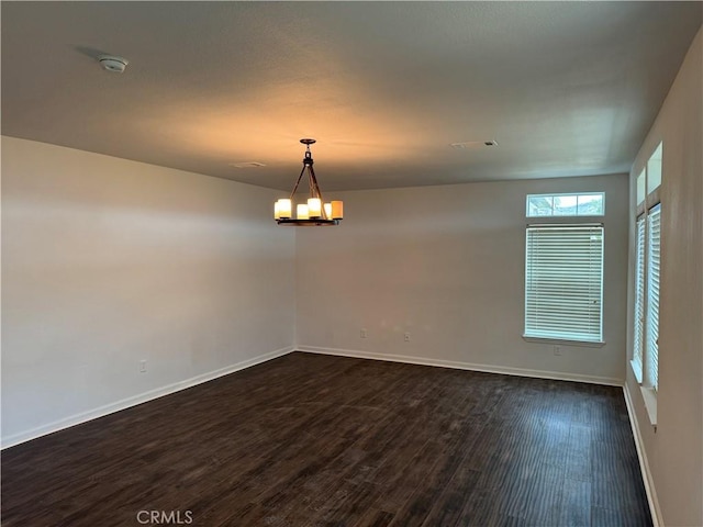 empty room featuring an inviting chandelier and dark wood-type flooring